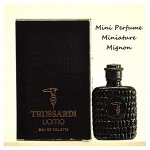 Peut inclure: Un flacon noir de parfum Trussardi Uomo Eau de Toilette avec un logo doré. Le flacon est étiqueté "Mini Parfum Miniature Mignon".
