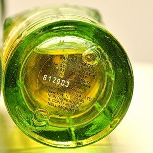 May include: Close-up of a green glass perfume bottle base with yellow liquid inside. The bottom of the bottle has printed text including "EAU DE TOILETTE" and "75 ml - 2.5 fl oz". The bottle is labeled "Versace Profumi".