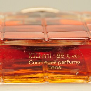 Puede incluir: Una botella de perfume de vidrio transparente con una tapa dorada. La botella est&aacute; llena de un l&iacute;quido marr&oacute;n rojizo. La etiqueta de la botella dice "100 ml 85% vol Courr&egrave;ges parfums paris".