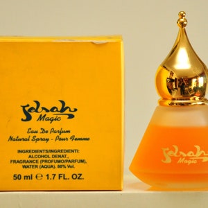May include: A yellow box with black text that reads "Sarah Magic Eau De Parfum Natural Spray - Pour Femme" and "INGREDIENTS/INGREDIENTI: ALCOHOL DENAT., FRAGRANCE (PROFUMO/PARFUM), WATER (AQUA). 80% Vol. 50 ml e 1.7 FL. OZ."  Next to the box is a clear glass bottle with a gold top and a yellow liquid inside. The bottle has black text that reads "Sarah Magic".