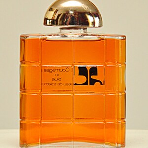 Puede incluir: Un frasco de perfume Coureges de vidrio transparente con una tapa dorada. El frasco est&aacute; lleno de un l&iacute;quido dorado y tiene un patr&oacute;n de cuadr&iacute;cula en la parte delantera. La etiqueta dice "Eau de Toilette, Blue in Coureges".