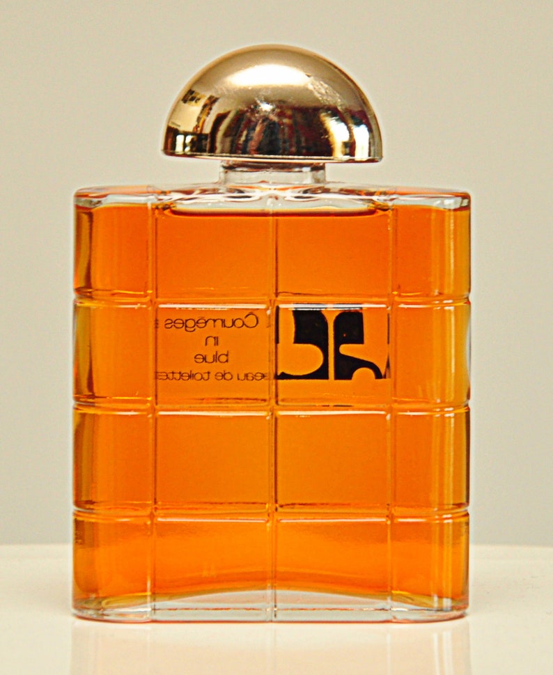 Puede incluir: Un frasco de perfume Coureges de vidrio transparente con una tapa dorada. El frasco est&aacute; lleno de un l&iacute;quido dorado y tiene un patr&oacute;n de cuadr&iacute;cula en la parte delantera. La etiqueta dice "Eau de Toilette, Blue in Coureges".