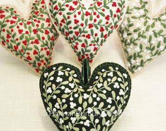 May include: Five heart-shaped decorations with floral patterns. The hearts display designs of red berries on white, white flowers on beige, and white flowers on a black background. Each ornament has a ribbon for hanging.
