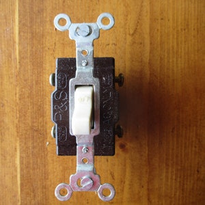 May include: A brown light switch with a white toggle switch labeled "OFF". The switch is mounted on a wooden surface and has metal mounting brackets.