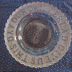 May include: A clear glass plate with a raised rim and a wheat sheaf design in the center. The rim is embossed with the words "Our Daily Bread".