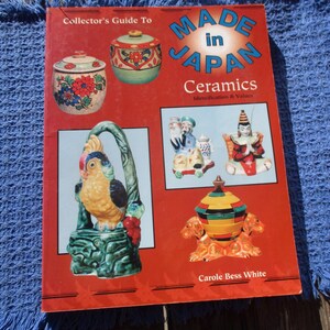 May include: A red book titled "Made in Japan Ceramics" with images of Japanese ceramic pieces. The cover features a variety of ceramic items, including decorative jars and figurines. The book is on a blue woven surface.
