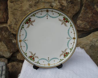 May include: A white porcelain plate with a gold rim and a decorative border of green, blue, and red floral designs.