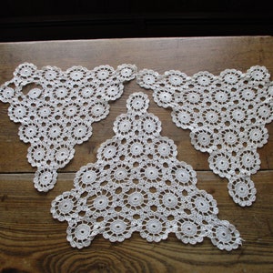 May include: Three white crocheted doilies in a triangular shape with a circular pattern.