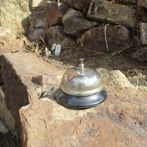 May include: A silver service bell with a black base sits on a large, rough, brown rock.