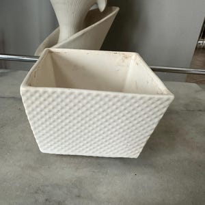 May include: White ceramic square planter with a textured surface. The planter is empty.