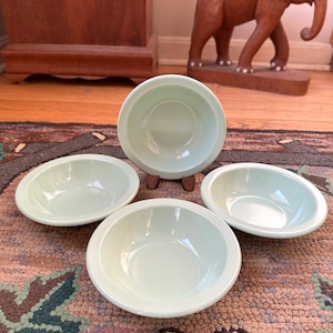 May include: Set of four light green ceramic bowls. The bowls are round and have a slightly raised rim.