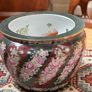 Puede incluir: Un cuenco redondo de cerámica con un borde verde oscuro y un cuerpo decorado con rayas diagonales alternas en verde oscuro y rojo intenso. Las rayas rojas están adornadas con motivos florales en tonos rosa, blanco y verde.