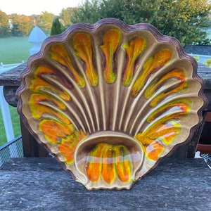 May include: A vintage, shell-shaped serving dish with a brown, scalloped rim. The interior features a tan base with vibrant orange and yellow accents. The dish has a central, rounded compartment, perfect for serving snacks or appetizers.