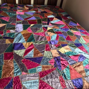 May include: A patchwork quilt featuring irregular, multi-colored fabric pieces in shades of magenta, teal, purple, gold, and blue. Each fabric segment is joined by visible, thick yellow cross-stitch embroidery, creating a textured, geometric surface.