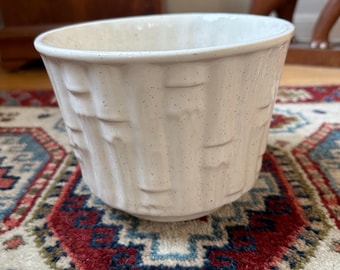 May include: A speckled, off-white ceramic planter with a textured, basket-weave design. The planter has a wide, slightly flared rim and a rounded base. This decorative container is suitable for indoor or outdoor use.
