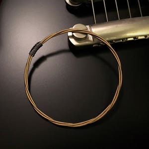 May include: A gold-colored guitar string bracelet with a silver clasp. The bracelet is made of multiple strands of string twisted together.