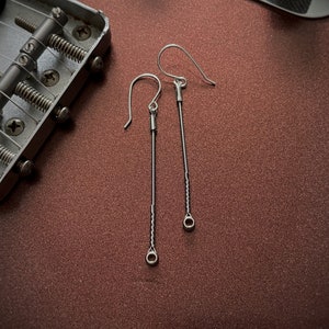 May include: A pair of silver dangle earrings with a long, thin chain and a small circle at the bottom.