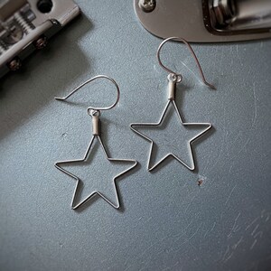 May include: A pair of silver star-shaped earrings with a simple wire design. The earrings have a hook closure.