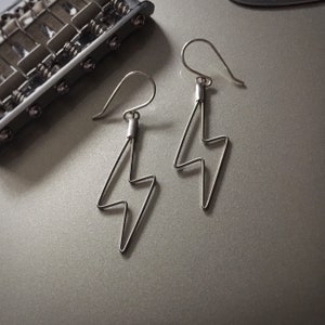 May include: A pair of silver lightning bolt earrings. The earrings are made of thin wire and have a simple, modern design.