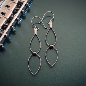 May include: A pair of silver earrings made from guitar strings. The earrings are shaped like teardrops and have a double loop design.