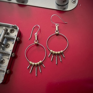 May include: A pair of silver hoop earrings with gold accents. The hoops are adorned with small gold rings and dangling silver spikes.