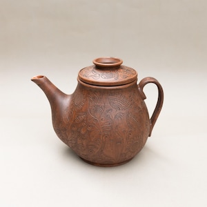 May include: A brown ceramic teapot with a lid, spout, and handle. The teapot features an embossed floral design. The teapot is a warm brown colour and appears to be handmade.