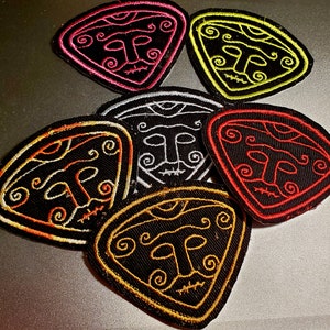 May include: Six embroidered iron-on patches in various colors, each featuring a stylized face with a third eye and swirling patterns. The patches are triangular in shape and have a black background.