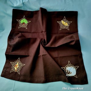 May include: A brown cloth altar cloth with four embroidered pentacles, each with a different element: a tree, a bird, a flame, and a wave. The pentacles are in the corners of the cloth.