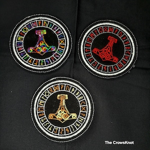 May include: Three embroidered patches with a circular design featuring a stylized hammer and runes around the edge. The patches are black with white outlines and the hammers are in different colors: rainbow, red, and gold.
