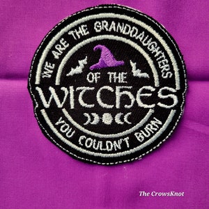 May include: A black and white embroidered patch with the text "We are the Granddaughters of the Witches You Couldn't Burn" and a purple witch's hat with bats on either side. The patch has three crescent moons in the center.