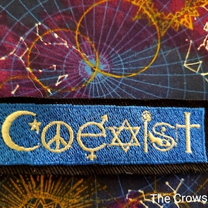 May include: A blue fabric patch with white embroidery of the word "Coexist" and symbols representing different religions, including a crescent moon and star, a peace sign, a yin-yang symbol, a Star of David, a Christian cross, and a Wiccan pentacle.
