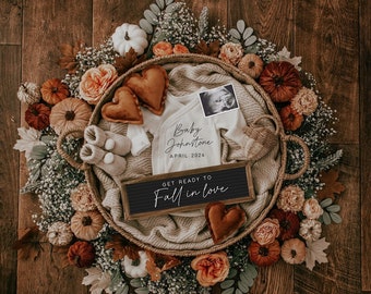 May include: A fall-themed baby announcement featuring a white onesie, a brown basket, and a sign that reads "Get ready to fall in love". The onesie has the text "Baby Johnston April 2024" printed on it. The basket is filled with autumnal-coloured flowers, leaves, and pumpkins.