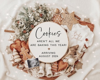 Pode incluir: Uma placa de madeira com o texto "Cookies aren't all we are baking this year!" e um coração. A placa também diz "Arriving August 2024". A placa é cercada por uma variedade de decorações natalinas, incluindo um homem de gengibre, uma pequena árvore de Natal, um macacão para bebê e uma estrela.