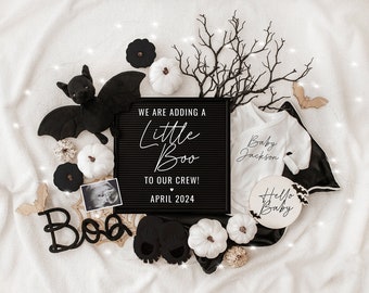 May include: A black letter board with the text "We are adding a little boo to our crew! April 2024".  A white onesie with the text "Baby Jackson" is next to the letter board.  There are white pumpkins, a black bat, and a wooden sign with the text "Hello Baby" in the image.