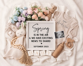 May include: A white letter board with the text "Spring is in the air & we have exciting news to share! September 2023".  The letter board is surrounded by baby items, including a onesie, a rattle, a wooden block that says "Baby", a stuffed bunny, and a bouquet of flowers.