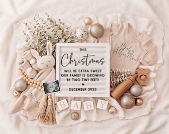 May include: A white signboard with black text announcing a baby is due in December 2023. The sign reads "This Christmas will be extra sweet our family is growing by two tiny feet!"  The sign is surrounded by baby items including a onesie, a stuffed bunny, wooden blocks spelling "BABY", and a wooden rattle.