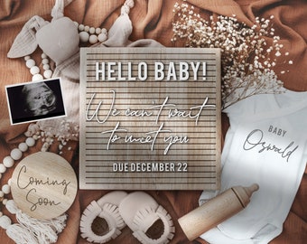 May include: A wooden sign with the text "Hello Baby! We can't wait to meet you. Due December 22."  A white onesie with the text "Baby Oswald" is next to the sign.  There are other baby items in the image, including a wooden circle with the text "Coming Soon", a pair of white booties, a wooden bottle, and a small ultrasound image.