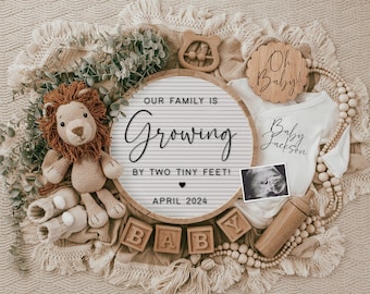 Peut inclure: Une pancarte en bois avec le texte "Notre famille s'agrandit de deux petits pieds ! Avril 2024" entourée d'articles pour bébés, dont un lion en tricot, une grenouillère, un hochet en bois et un bloc en bois qui épelle "BABY".
