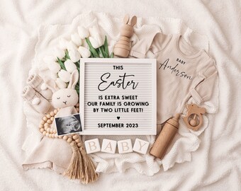 May include: A white letter board with the text "This Easter is extra sweet our family is growing by two little feet! September 2023".  The letter board is surrounded by baby items, including a white onesie with the text "Baby Anderson", a wooden bunny, a wooden rattle, a wooden bottle, a beaded garland with an ultrasound image, and a set of wooden blocks that spell "BABY".