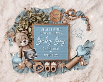 May include: A blue and white letter board with the text "We are excited to say we have a Baby Boy on the way! April 2025". The board is surrounded by baby items, including a crocheted teddy bear, a onesie, booties, and a wooden rattle.