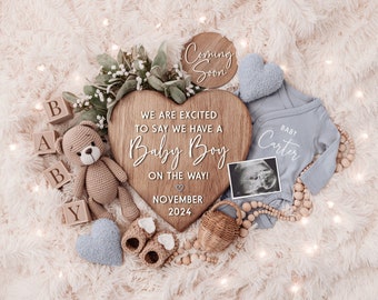 Puede incluir: Un letrero de madera en forma de corazón con el texto "We are excited to say we have a Baby Boy on the way! November 2024". El letrero está rodeado de artículos para bebés, incluyendo un mameluco azul con el texto "Baby Carter", un osito de peluche, bloques de madera que deletrean "BABY", una pequeña cesta de mimbre y una almohada azul en forma de corazón.