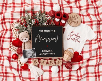 Op de afbeelding: Een zwart schoolbord met de tekst "The more the merrier! Arriving August 2025". Het bord is omringd door rood-wit geruit stof, een teddybeer, een baby-romper, een houten blok dat "BABY" spelt, en andere kerstversiering.