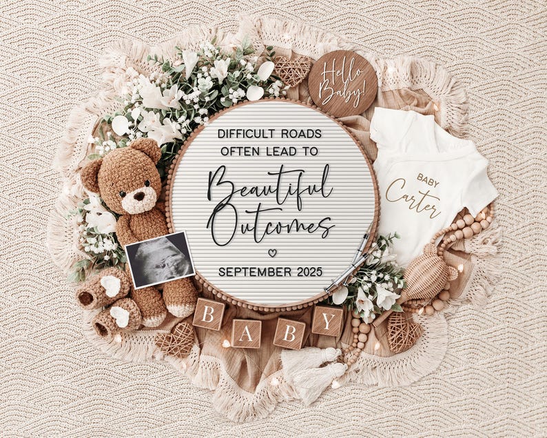 May include: A white letter board with the text "Difficult roads often lead to beautiful outcomes" and the date "September 2025". The board is surrounded by a teddy bear, baby booties, a baby onesie, and wooden blocks that spell out "BABY".