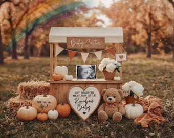 May include: A fall-themed pregnancy announcement with a wooden stand, pumpkins, and a teddy bear. The stand has a sign that reads "Baby Carter" and a heart-shaped sign that says "Get Ready to Meet Our Little Rainbow Baby." A pumpkin says "See You in April."