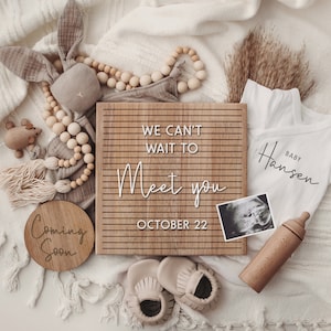 K&ouml;nnte beinhalten: Ein Holz-Buchstabenbrett mit dem Text "We can't wait to meet you October 22".  Um das Brett herum befinden sich Babyartikel wie ein Strampler, eine Holzrassel, eine Holzbabyflasche, eine Holzperlenkette, ein Paar Babyschuhe und ein Ultraschallbild.