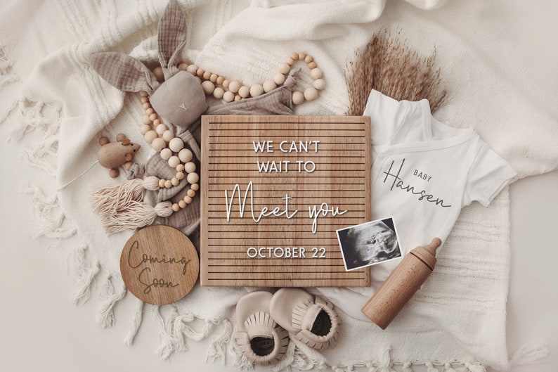 K&ouml;nnte beinhalten: Ein Holz-Buchstabenbrett mit dem Text "We can't wait to meet you October 22".  Um das Brett herum befinden sich Babyartikel wie ein Strampler, eine Holzrassel, eine Holzbabyflasche, eine Holzperlenkette, ein Paar Babyschuhe und ein Ultraschallbild.