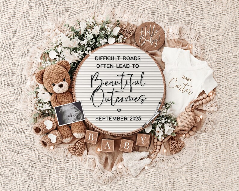 May include: A white letter board with the text "Difficult roads often lead to beautiful outcomes" and the date "September 2025". The board is surrounded by a teddy bear, baby booties, a baby onesie, and wooden blocks that spell out "BABY".