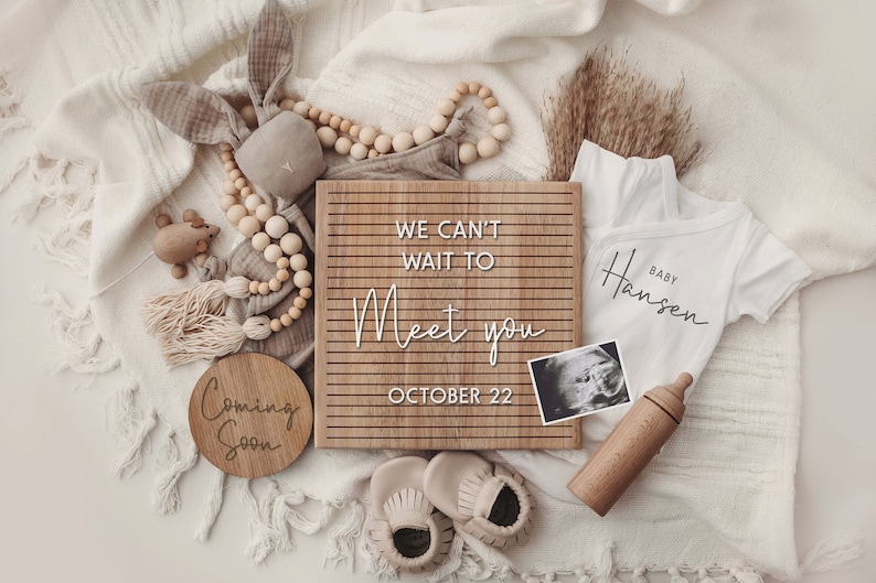 K&ouml;nnte beinhalten: Ein Holz-Buchstabenbrett mit dem Text "We can't wait to meet you October 22". Es gibt einen Baby-Strampler mit dem Text "Baby Hansen", eine Holz-Babyflasche, ein Holzschild mit der Aufschrift "Coming Soon", ein Holzspielzeug und ein kleines Ultraschallbild.