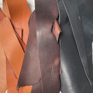 Puede incluir: Surtido de tiras de cuero en colores marrón, marrón oscuro y negro. El cuero es texturizado y parece estar cortado en varias formas y tamaños.