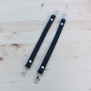 May include: Two black leather straps with silver swivel clasps. The straps are approximately 30 cm long.